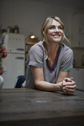 Portrait of happy woman leaning on kitchen table - RBF06199