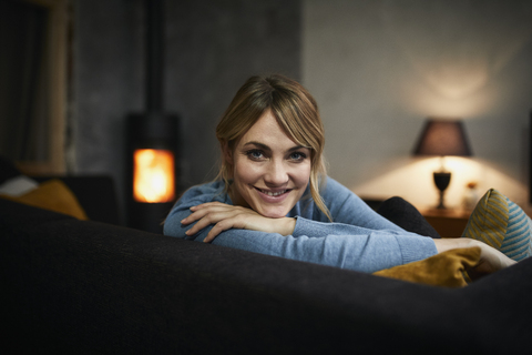 Portrait of smiling woman relaxing on couch at home in the evening stock photo