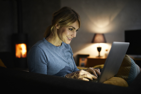 Smiling woman using laptop at home in the evening stock photo