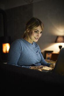 Porträt einer lächelnden Frau, die abends zu Hause einen Laptop benutzt - RBF06208