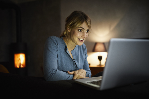 Porträt einer verblüfften Frau, die abends zu Hause einen Laptop benutzt, lizenzfreies Stockfoto