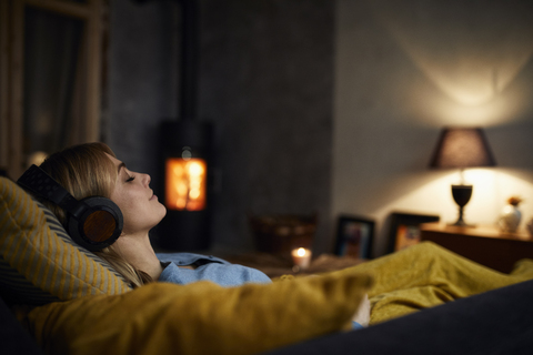 Smiling woman listening music with headphones on couch at home in the evening stock photo