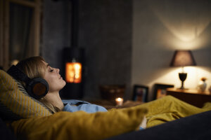 Lächelnde Frau hört Musik mit Kopfhörern auf der Couch zu Hause am Abend - RBF06210