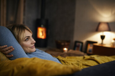 Smiling woman relaxing on couch at home in the evening - RBF06213