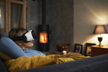 Frau liegt abends zu Hause auf der Couch und benutzt eine Virtual-Reality-Brille - RBF06214