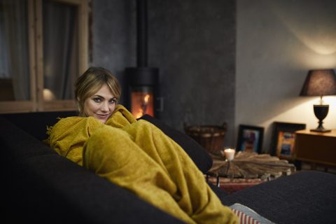 Porträt einer lächelnden Frau, die sich abends zu Hause auf der Couch entspannt, lizenzfreies Stockfoto