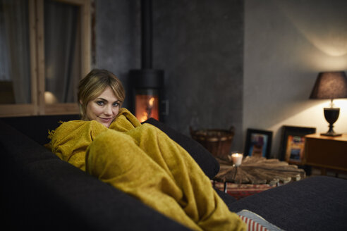 Porträt einer lächelnden Frau, die sich abends zu Hause auf der Couch entspannt - RBF06216