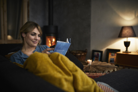 Portrait of smiling woman reading a book on couch at home in the evening stock photo