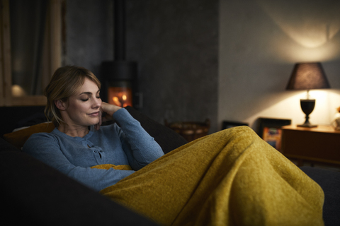 Portrait of smiling woman relaxing on couch at home in the evening stock photo