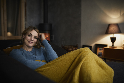 Porträt einer glücklichen Frau, die sich abends zu Hause auf der Couch entspannt, lizenzfreies Stockfoto