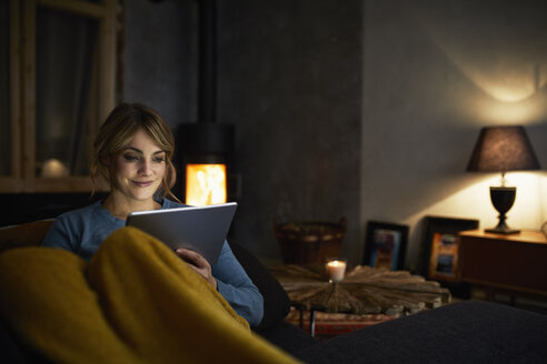 Porträt einer lächelnden Frau mit Tablet entspannt auf der Couch am Abend - RBF06223