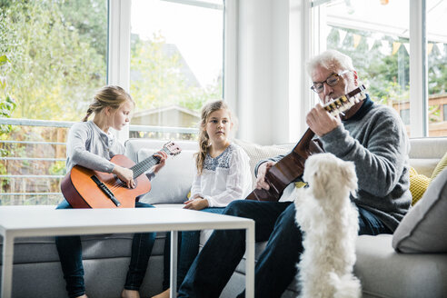 Zwei Mädchen und Großvater auf dem Sofa spielen Gitarre und der Hund schaut zu - MOEF00518