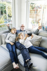 Two girls and grandfather on sofa taking a selfie - MOEF00520