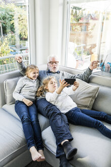 Zwei Mädchen und Großvater auf dem Sofa machen ein Selfie - MOEF00520