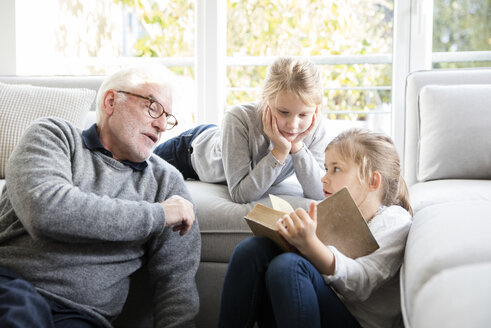 Zwei Mädchen und Großvater lesen ein Buch im Wohnzimmer - MOEF00524