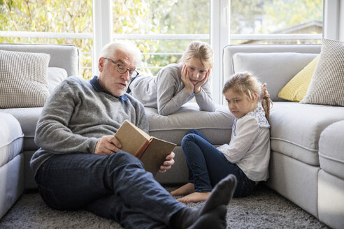 Zwei Mädchen und Großvater lesen ein Buch im Wohnzimmer - MOEF00527