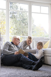 Zwei Mädchen und Großvater lesen ein Buch im Wohnzimmer - MOEF00529
