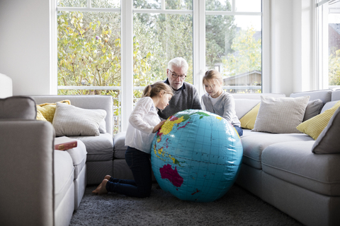 Zwei Mädchen und Großvater mit Globus im Wohnzimmer, lizenzfreies Stockfoto