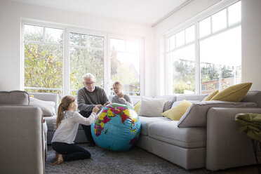 Two girls and grandfather with globe in living room - MOEF00531