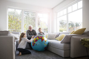 Zwei Mädchen und Großvater mit Globus im Wohnzimmer - MOEF00531