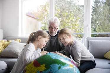 Zwei Mädchen und Großvater mit Globus im Wohnzimmer - MOEF00532