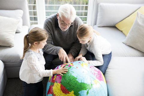 Two girls and grandfather with globe in living room stock photo