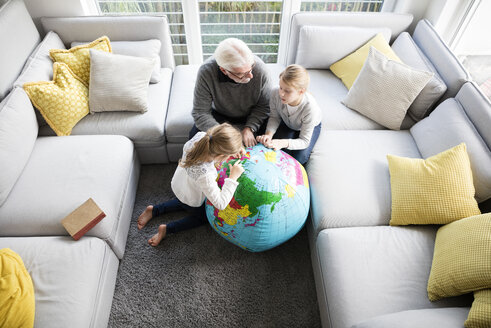 Zwei Mädchen und Großvater mit Globus im Wohnzimmer - MOEF00534