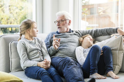 Grandfather talking to two girls on sofa in living room stock photo