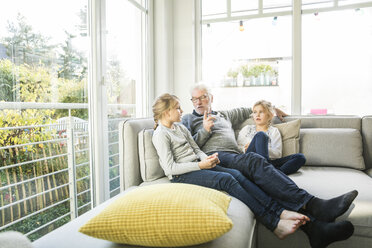 Grandfather talking to two girls on sofa in living room - MOEF00537