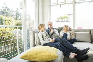 Großvater im Gespräch mit zwei Mädchen auf dem Sofa im Wohnzimmer - MOEF00537