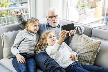 Zwei Mädchen und Großvater auf dem Sofa machen ein Selfie - MOEF00538