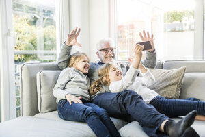 Zwei glückliche Mädchen und Großvater auf dem Sofa machen ein Selfie - MOEF00539