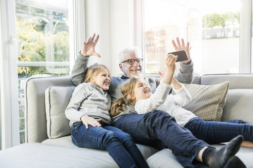 Zwei glückliche Mädchen und Großvater auf dem Sofa machen ein Selfie - MOEF00539