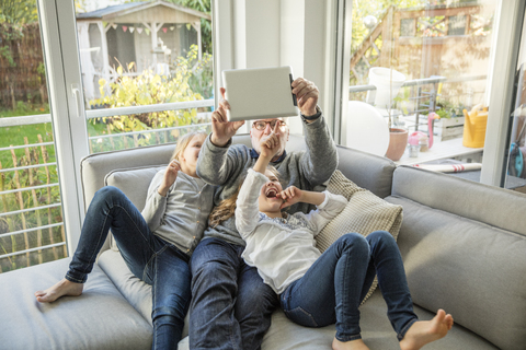 Two happy girls and grandfather on sofa taking a selfie with tablet stock photo