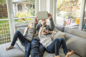 Zwei glückliche Mädchen und Großvater auf dem Sofa machen ein Selfie mit Tablet - MOEF00540