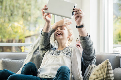 Zwei glückliche Mädchen und Großvater auf dem Sofa machen ein Selfie mit Tablet - MOEF00542