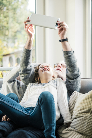 Zwei glückliche Mädchen und Großvater auf dem Sofa machen ein Selfie mit Tablet, lizenzfreies Stockfoto