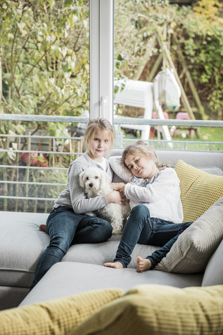 Portrait of two girls with dog on couch in living room stock photo