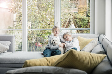 Porträt von zwei Mädchen mit Hund auf der Couch im Wohnzimmer - MOEF00545