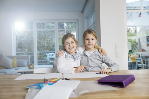 Porträt von zwei sich umarmenden Mädchen, die gemeinsam am Tisch Hausaufgaben machen, lizenzfreies Stockfoto