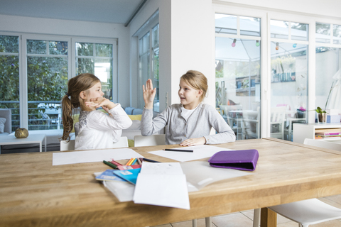 Zwei Mädchen machen Hausaufgaben am Tisch zusammen High Fiving, lizenzfreies Stockfoto