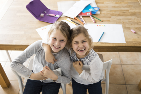 Portrait of two happy girls embracing at table together stock photo