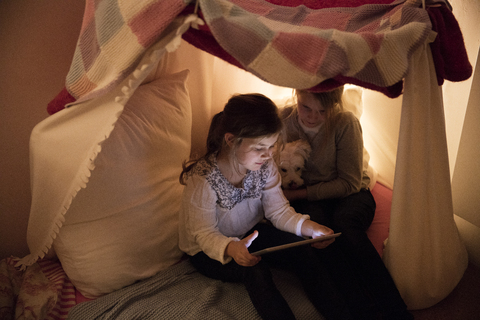 Zwei Mädchen mit Hund und Tablet im Kinderzimmer, lizenzfreies Stockfoto