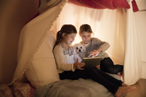 Zwei Mädchen mit Hund und Tablet im Kinderzimmer, lizenzfreies Stockfoto