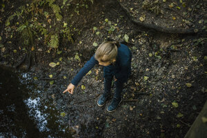 Mädchen in einem Wald an einem Teich stehend und mit dem Finger zeigend - MOEF00570