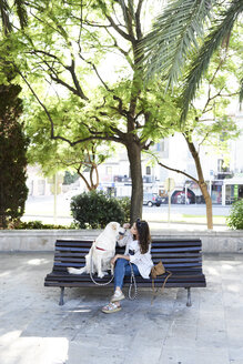 Junge Frau sitzt auf einer Bank mit ihrem Hund in der Stadt - IGGF00316