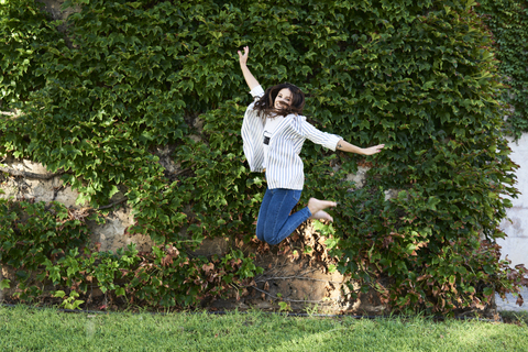 Happy young woman jumping in the air outdoors stock photo