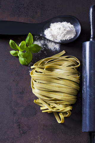 Green Tagliatelle, spoon of flour, basil leaves and rolling pin on rusty ground stock photo