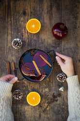 Woman's hands holding cooking pot of mulled wine with orange slices and spices - LVF06544