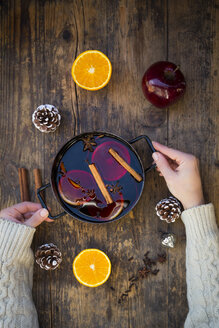 Frauenhände halten einen Kochtopf mit Glühwein, Orangenscheiben und Gewürzen - LVF06544